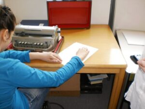 Kind sitzend am Schreibtisch mit Blindenschreibmaschine